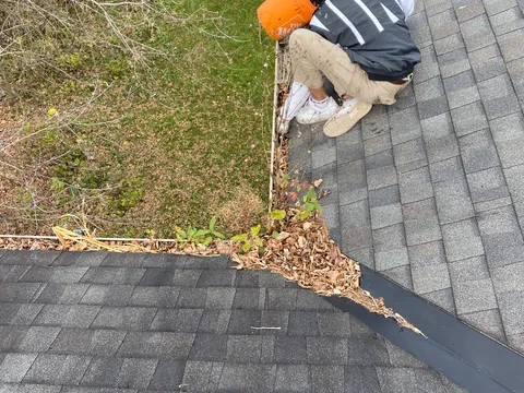 Technicien retirant les débris d'une gouttière à la main sur un toit résidentiel à Gatineau