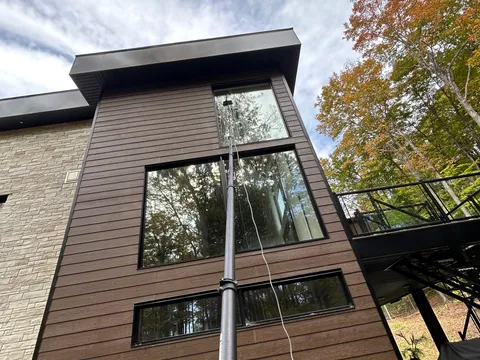 Technicien utilisant une perche télescopique à eau pure pour laver les fenêtres d'une résidence à étages à Gatineau