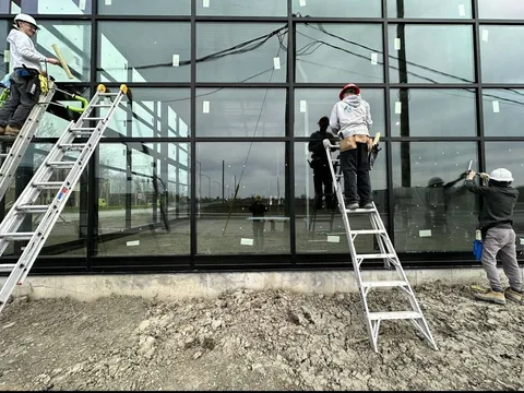 Équipe nettoyant les grandes vitres d'un bâtiment neuf, étiquettes de protection encore sur le verre, chantier presque terminé